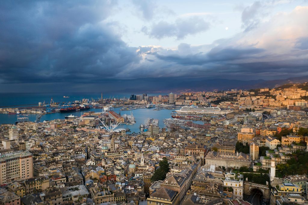 A stunning aerial view of Genova, Italy, showcasing its urban landscape and harbor at dusk under a cloudy sky.