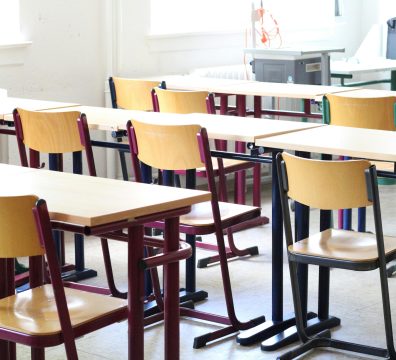 A bright empty classroom with wooden tables and chairs, ready for students.