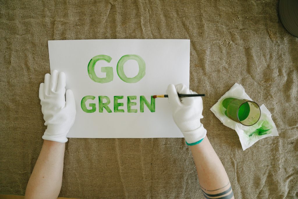 Overhead view of go green poster creation with paint and gloves on natural fabric background.