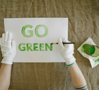 Overhead view of go green poster creation with paint and gloves on natural fabric background.