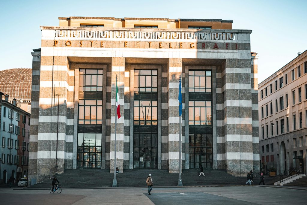 Front view of the historic Italian post office building in Brescia, Italy, with flags and pedestrians.