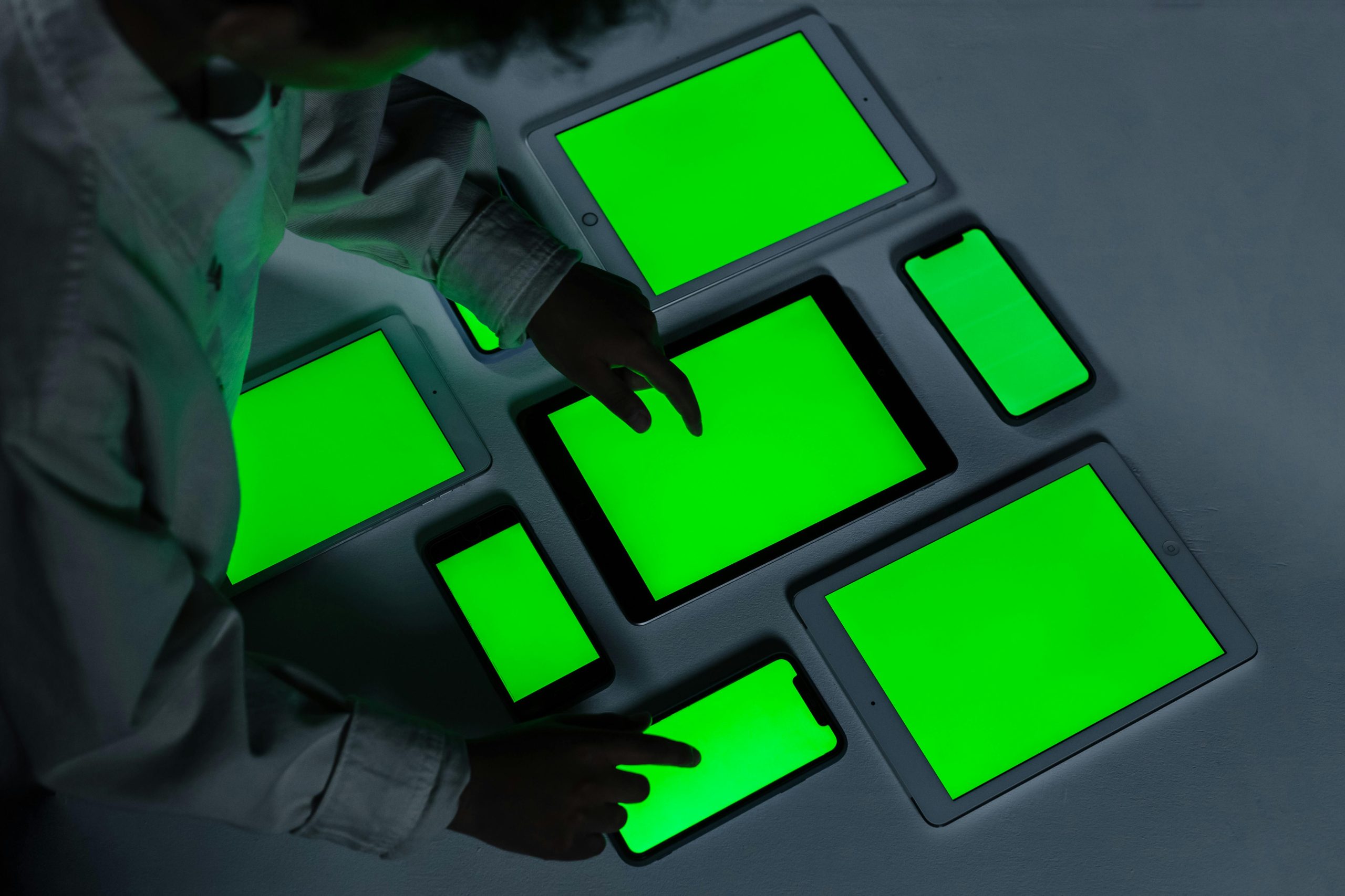 A variety of electronic gadgets with green screens being interacted with indoors.