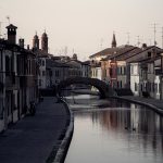 Charming canal scene in Comacchio, Italy featuring historical architecture and a serene water reflection.