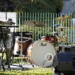 An outdoor music stage setup featuring a drum set and keyboard, ready for a live performance.