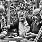 Four elderly men enjoy a game of cards outdoors in a Turkish café setting, captured in black and white.