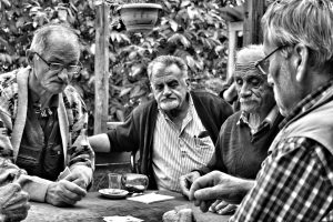 Four elderly men enjoy a game of cards outdoors in a Turkish café setting, captured in black and white.