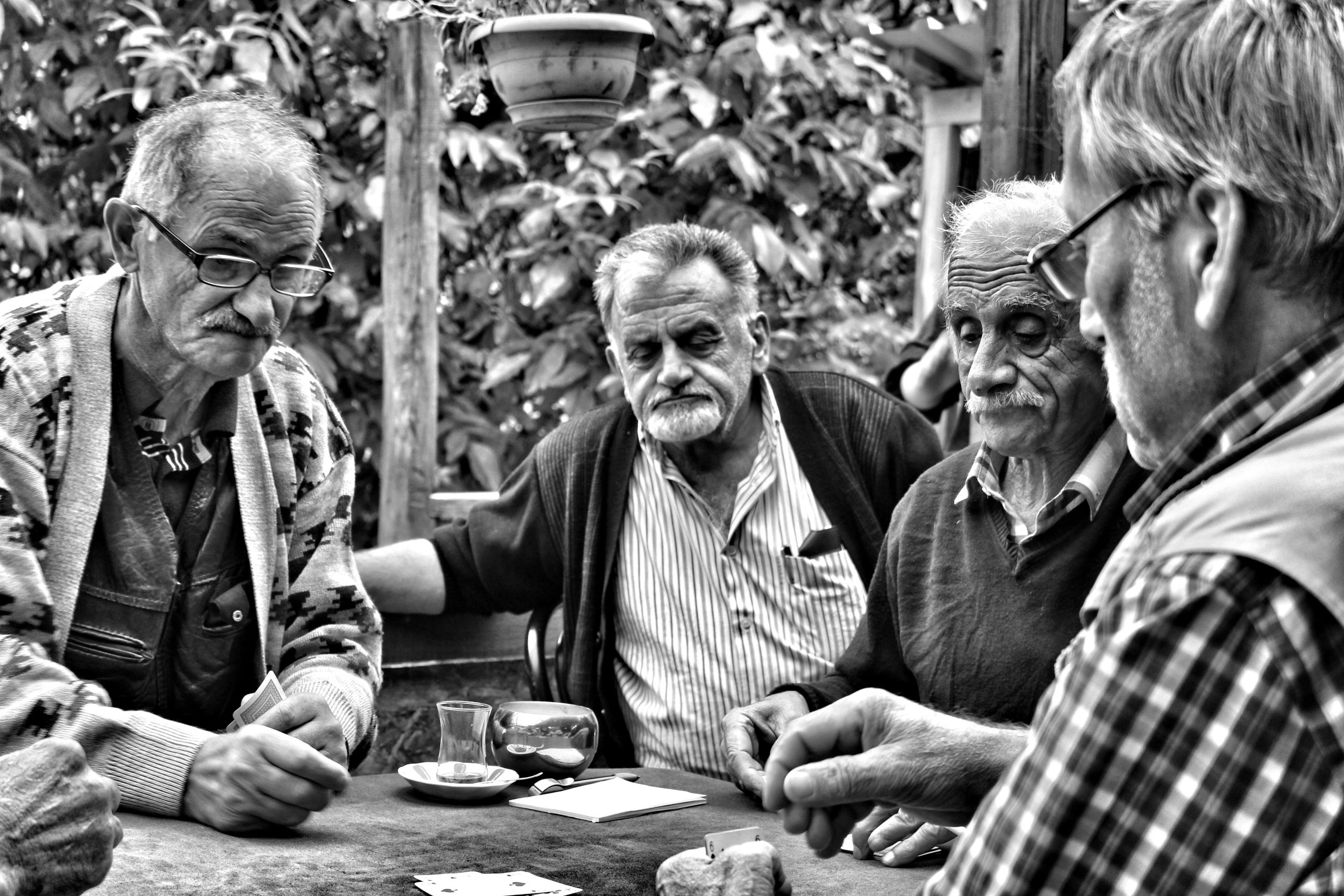 Four elderly men enjoy a game of cards outdoors in a Turkish café setting, captured in black and white.