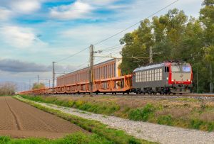 Cargo train on a railway cutting through rural Caserta, Italy, amidst lush greenery and open fields.