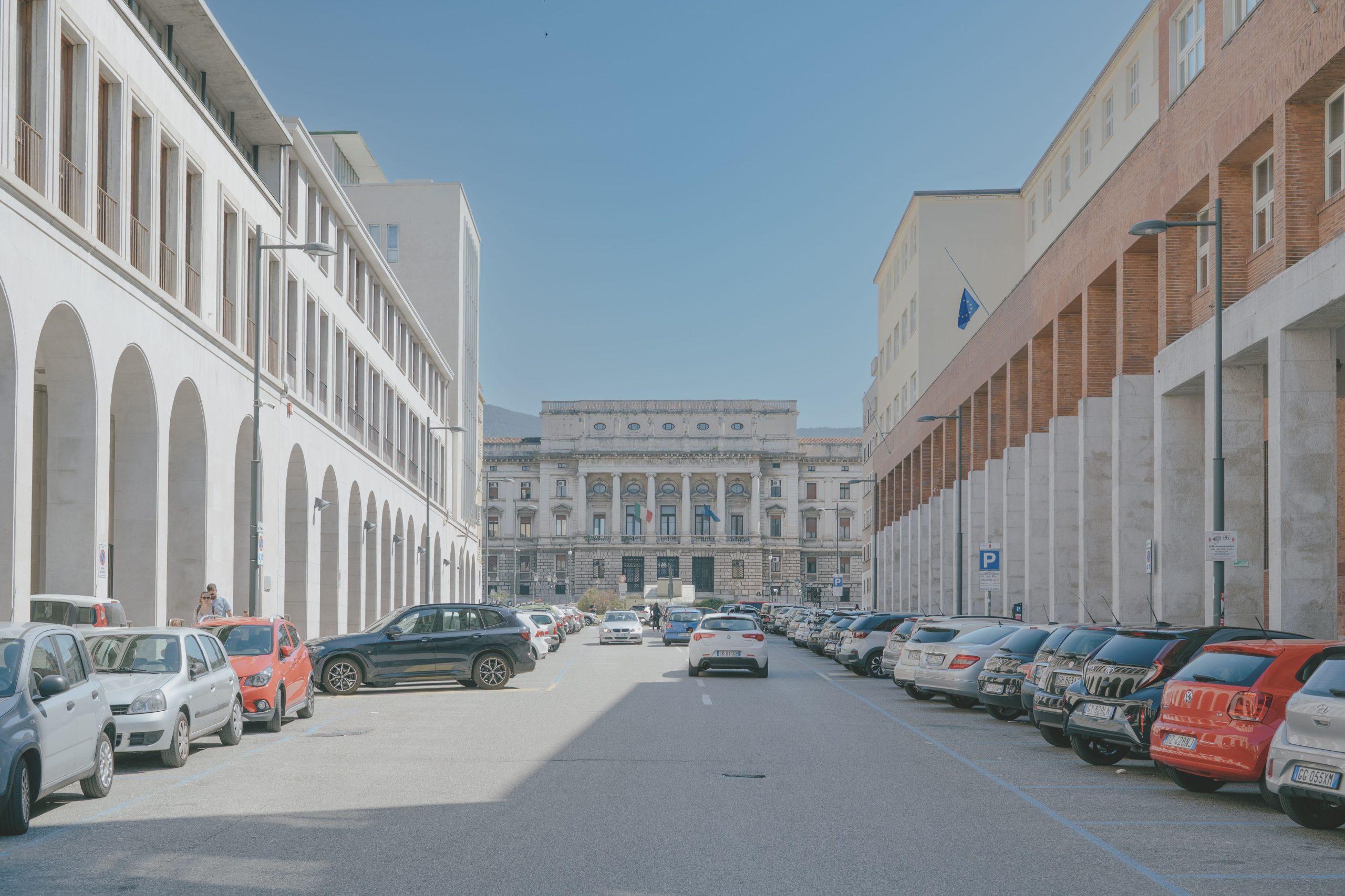 Central street view with historic architecture and parked cars in Trieste, showcasing urban Italian scenery.