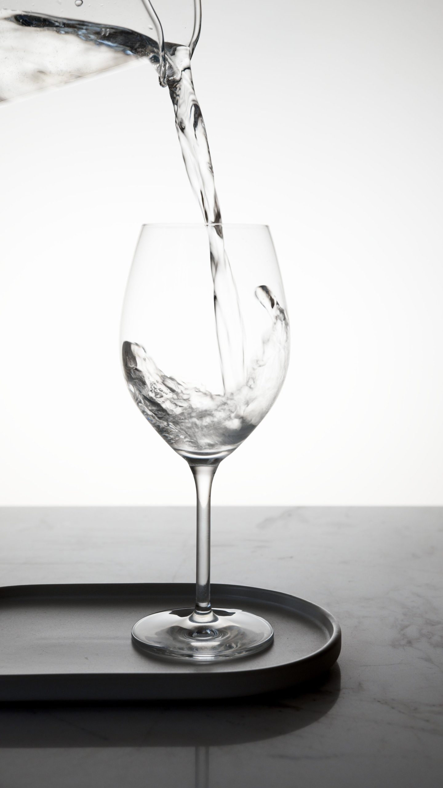 Minimalist image of clear water being poured into a wine glass on a marble surface.