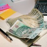 A stack of Polish Zloty banknotes on an office table with a calculator and notebook.