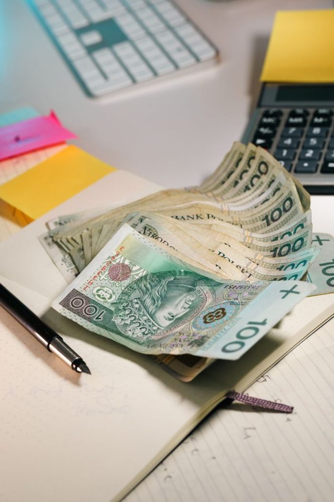 A stack of Polish Zloty banknotes on an office table with a calculator and notebook.